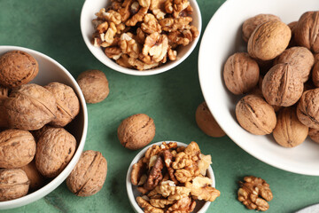 Bowls with tasty walnuts on green background