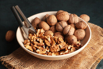 Bowl with tasty walnuts and nutcracker on dark background