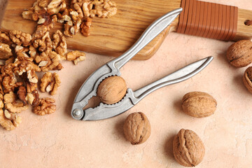 Wooden board with tasty walnuts and nutcracker on beige background