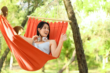 Naklejka premium Young woman with headphones relaxing in hammock outdoors