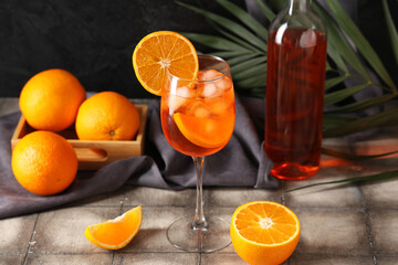 Glass of Aperol spritz cocktail with fruits and palm leaf on grey tile table
