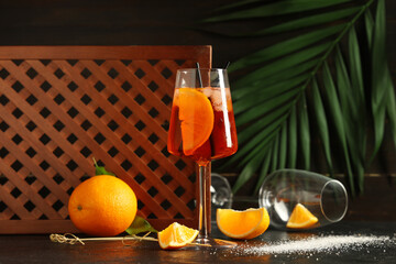 Glass of Aperol spritz cocktail and palm leaf on black table