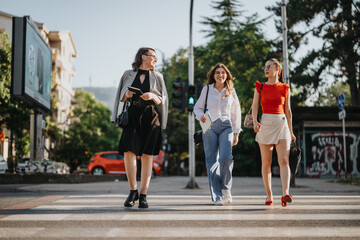 Three stylish businesswomen walking across a city street, enjoying the sunny day and each other's company.