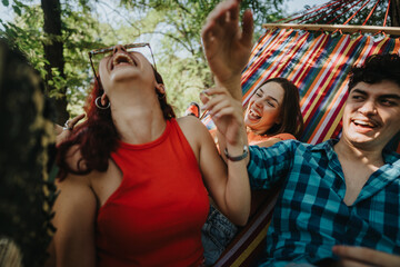 Group of friends having a great time, laughing and relaxing on a colorful hammock in a lush outdoor setting.