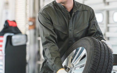 自動車整備工場でタイヤを運ぶ男性メカニック（肉体労働・重労働・重い・腰痛）  © buritora