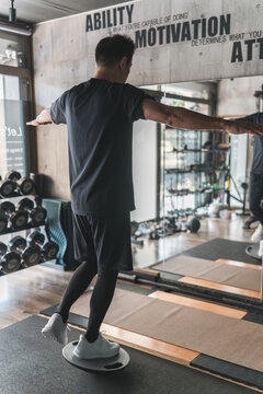 スーツジムでバランスボードに乗って体幹トレーニングする男性の後ろ姿
