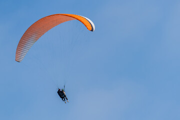 An orange-and-white paraglider flying in the sky