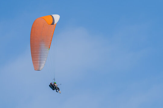 An orange-and-white paraglider flying in the sky