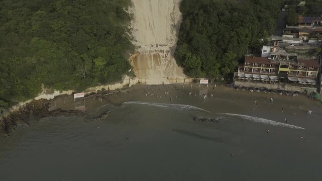 Drone flies backwards from Ponta Negra beach at base of Morro do Careca in Natal, Rio Grande do Norte, Brazil