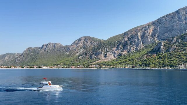 View of &Ouml;ren holiday resort from a beach tour boat, highlighting impressive mountain range and small motor yacht underway calm waters. Tranquil scene captures beauty of nature. Milas, Turkey
