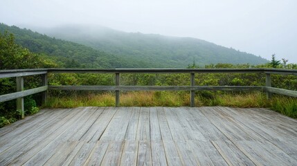 Fototapeta premium A wooden deck offers a serene view of fog-laden mountains and lush greenery.