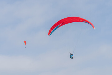 Two red paragliders meet in the sky.