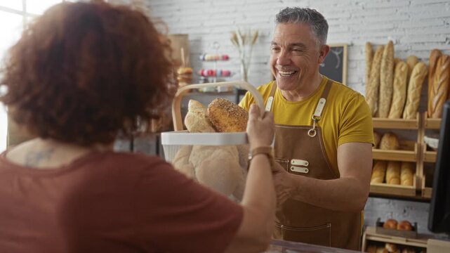 Smiling baker presenting bread basket to woman in modern bakery with shelves of baked goods in background