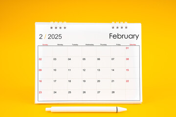 February 2025, Monthly desk calendar for 2025 year and pen on yellow background.