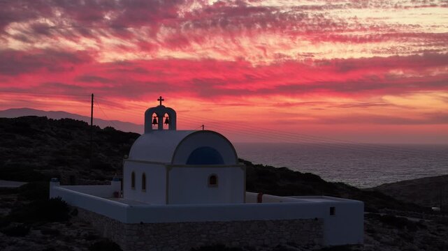 Fire red clouds contrast against Holy Wisdom church in Donousa Greece at sunset
