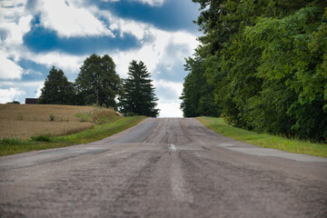 Empty countryside road with lush green trees and blue sky with clouds