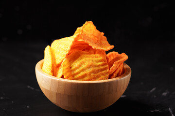 Wave-cut cassava chips, fried to a crispy texture, orange in color, and coated with a savory, spicy-sweet seasoning. Photographed against a dark background.
