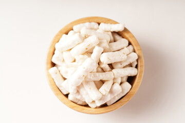 A bowl of small, white tube-shaped crackers with a savory, spicy flavor. Photographed against a white background.