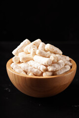 A bowl of small, white tube-shaped crackers with a savory, spicy flavor. Photographed against a dark background.