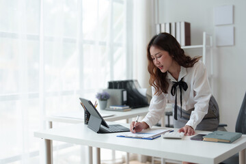 Happy Asian businesswoman in office working on financial documents, checking, validating data on laptop, results, income, online marketing.  Company taxes Online business work.