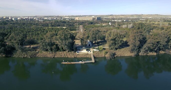 Drone video that begins its flight over the Guadalquivir River and continues over the Alamillo Park with different species of trees and in the background you can see the Olympic Stadium of La Cartuja.
