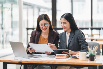 Two young Asian businesswomen discuss new startup project idea, analyzing planning and financial statistics, investment market, at the office.