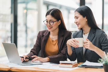 Two young Asian businesswomen discuss new startup project idea presentation, analyzing planning, financial statistics, and investment market at office.