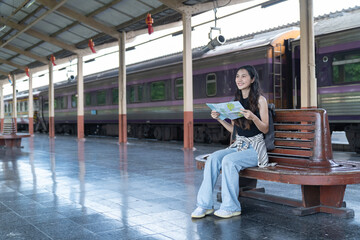 young woman is walking with suitcase at railway station, using the smartphone and map, traveling by train.