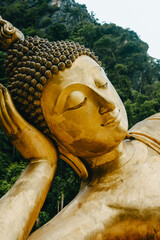 Vertical image of huge gold Reclining Buddha statue with mountain background inThailand.
