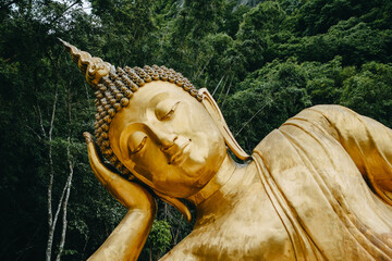 Close up of Reclining Buddha gold statue face with mountain background inThailand.