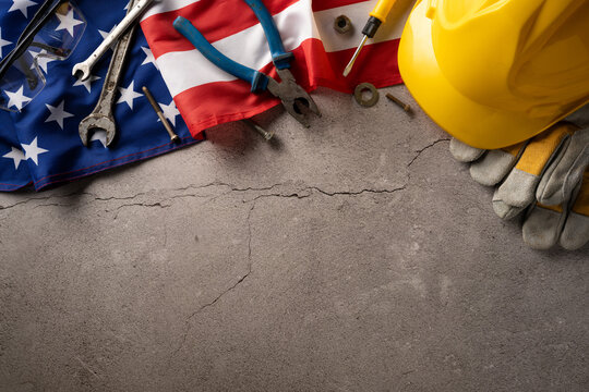 Top view of various tools, American flag, hard hat, and gloves on a cracked concrete surface for Labor Day - Powered by Adobe