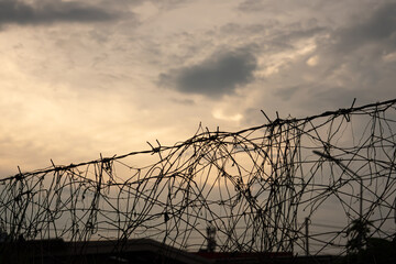 A wire fence with a lot of barbed wire on it. The sky is cloudy and the sun is setting