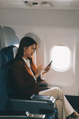 Young asian woman sitting on seat in airplane and talking by smartphone. Young woman traveller talking on cell phone