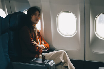 Photo of a frustrated woman sitting on an airplane with her head in her hands. Asian woman sitting...