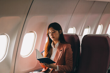 Attractive Asian female passenger of airplane sitting in comfortable seat while working laptop and...
