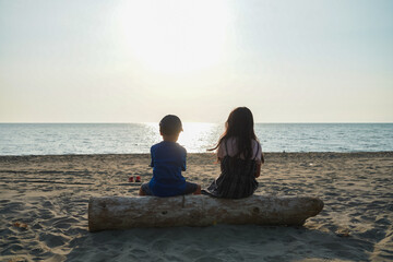 海辺の切られた木の上に座る二人の子供の後ろ姿