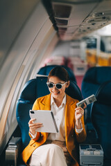 Naklejka premium A young Asian woman, seated as an airplane passenger, contemplates dollar bills, reflecting on lucrative opportunities and aspirations towards billionaire status.