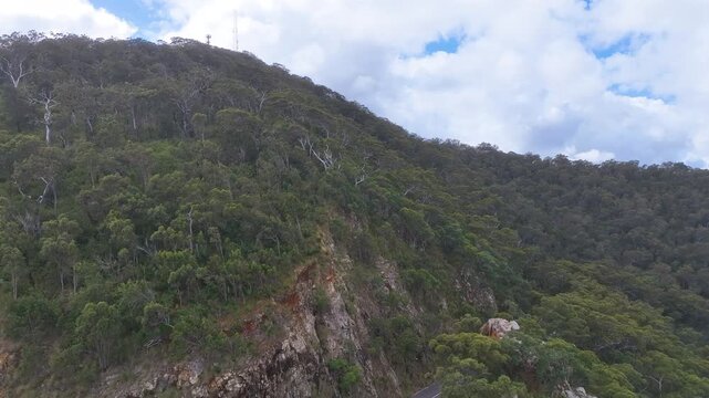 Aerial above two cars parked at Sleipner Lookout above Rockhampton Queensland and Pilbeam Drive leading to the summit of famed Mount Archer in the National Park. Aerial shows coloured rock cutting.