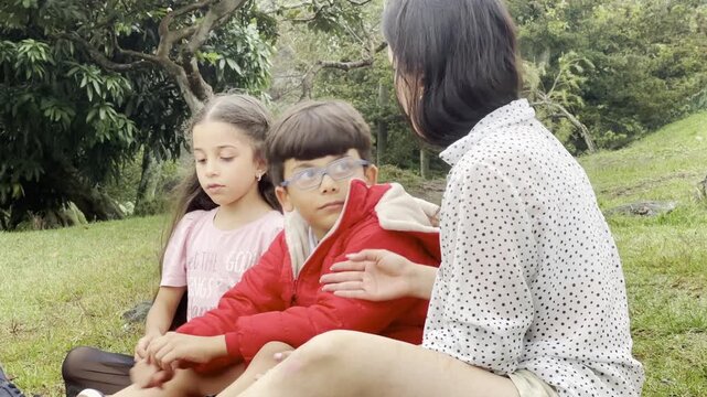 International Children Day. Latin mother having fun with her young children outdoors. Sitting on the ground playing with their hands. Concept of family. Single mother with two young children.
