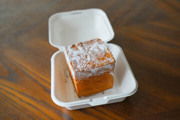 A cube toast, on a wooden table, topped with sugar powder, Takeaway food.