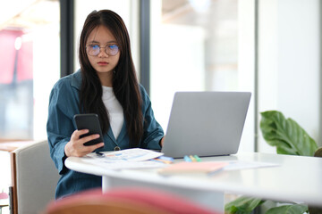 A woman is sitting at a table with a laptop and a cell phone