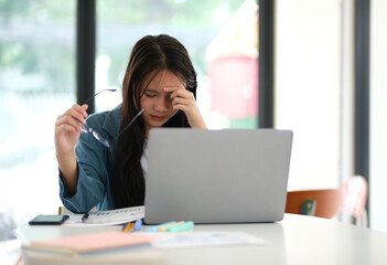 Obraz premium A woman is sitting at a table with a laptop and a stack of papers