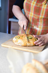 Person slicing a jalape&ntilde;o-topped loaf of bread on a cutting bo