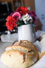 Freshly baked rustic bread loaf with a vase of colorful flowers