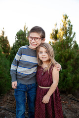 Smiling boy and girl standing outdoors in front of pine trees