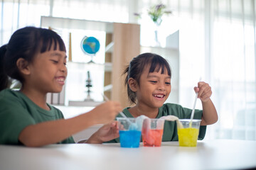 Two young girls are sitting at a table, playing with a science experiment