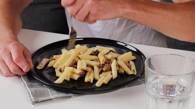 A man impales feather pasta on a fork as he eats.