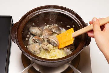 土鍋で玉ねぎ、ニンニク、アサリを炒めパエリアを作る