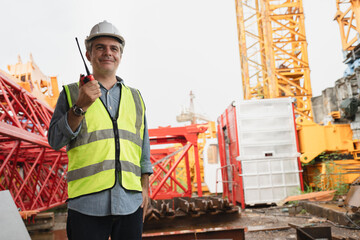 Caucasian mature engineer man worker use tablet computer and walkie talkie working with spare crane background	