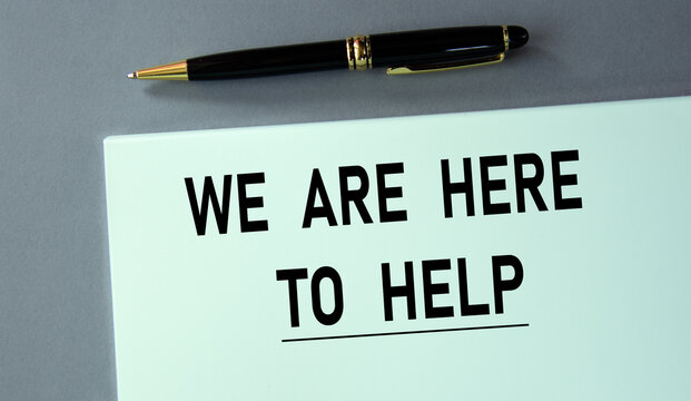 WE ARE HERE TO HELP - words on a piece of paper with a pen on a gray background